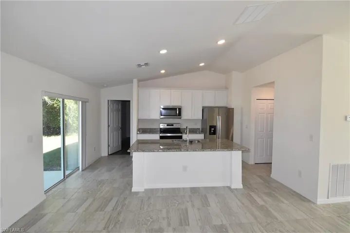 Kitchen with stainless steel appliances, white cabinetry, lofted ceiling, dark stone counters, and a kitchen island with sink