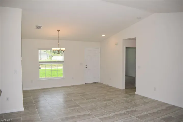 Tiled empty room with vaulted ceiling and a notable chandelier