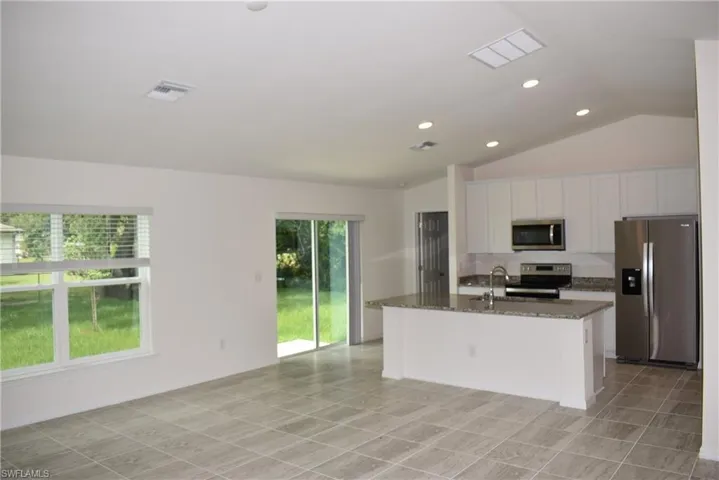 Kitchen with lofted ceiling, light tile patterned floors, dark stone counters, an island with sink, and stainless steel appliances