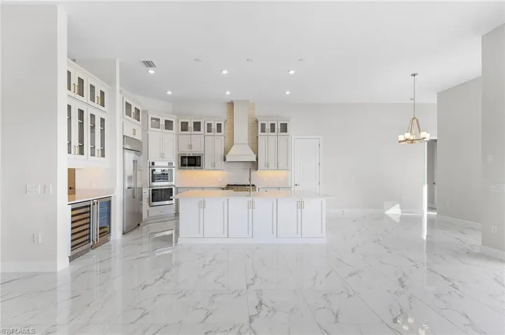 Kitchen with built in appliances, baseboards, wine cooler, and wall chimney range hood
