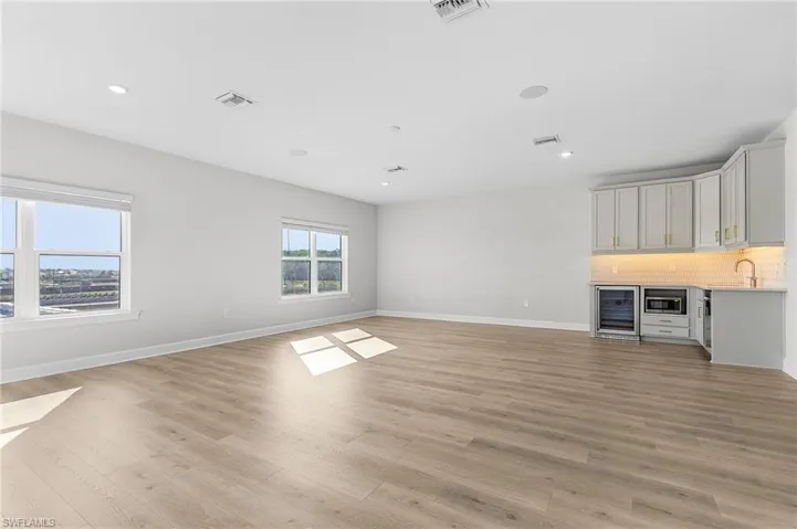 Unfurnished living room with beverage cooler, baseboards, visible vents, and light wood-style flooring