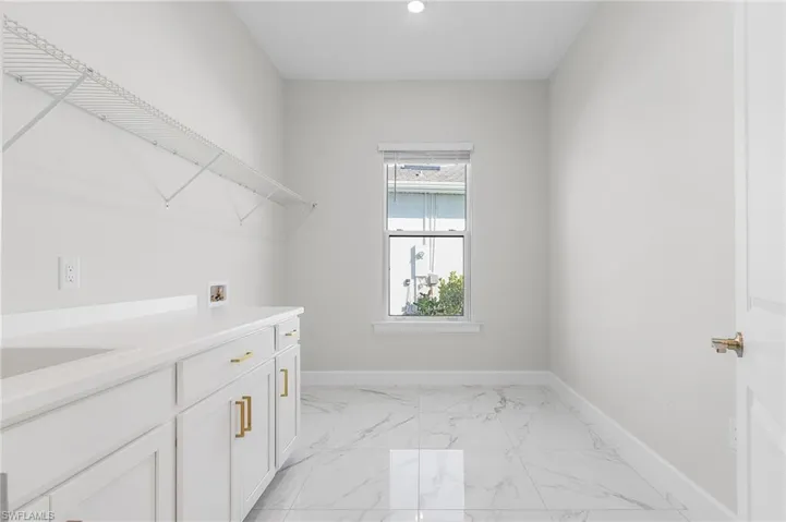 Clothes washing area with baseboards, marble finish floor, washer hookup, and cabinet space