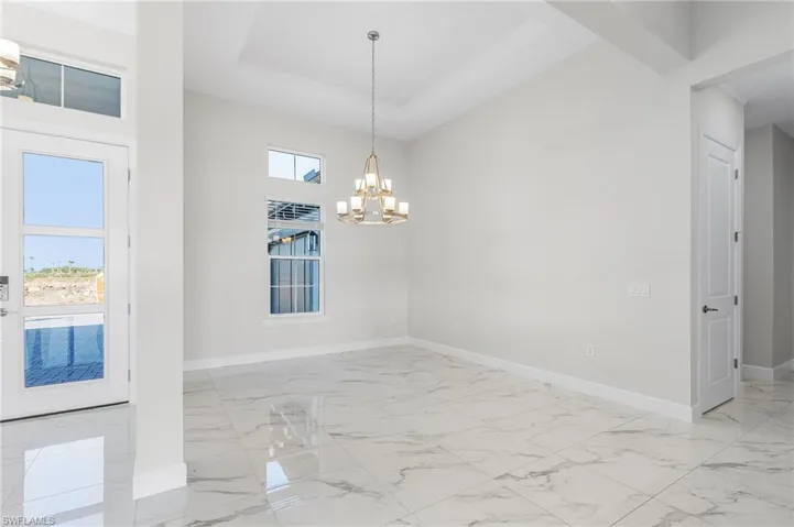 Empty room with a chandelier, a towering ceiling, baseboards, a raised ceiling, and marble finish floor