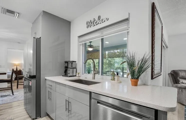 Kitchen with stainless steel appliances, light stone counters, light wood-style floors, gray cabinets, and a ceiling fan