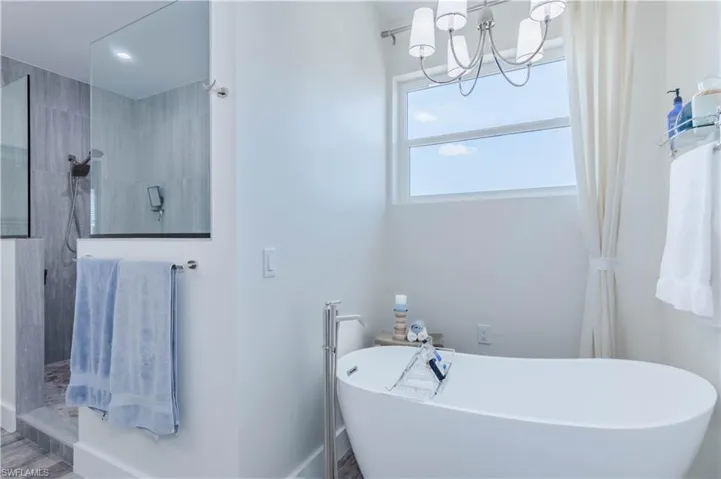 Bathroom featuring a soaking tub, a notable chandelier, and a walk in shower
