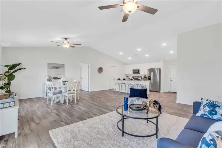 Living area with baseboards, light wood-type flooring, vaulted ceiling, and a ceiling fan
