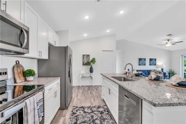 Kitchen with white cabinetry, a sink, appliances with stainless steel finishes, and lofted ceiling