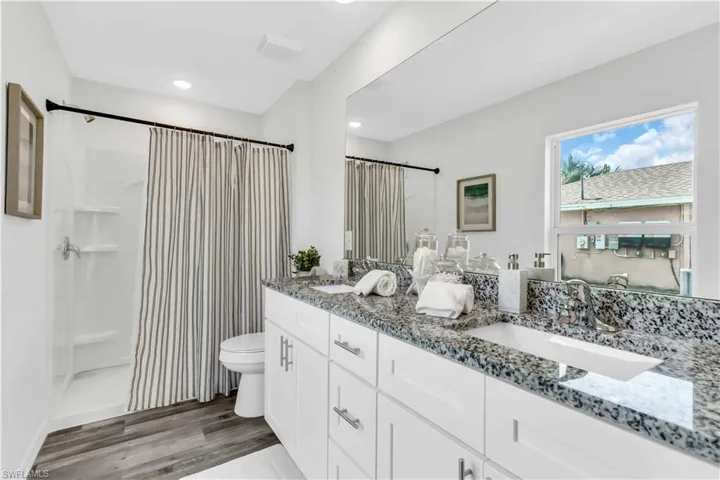 Bathroom featuring double vanity, toilet, wood finished floors, a shower with curtain, and a sink