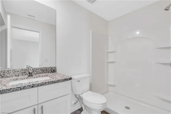 Bathroom with a stall shower, visible vents, toilet, and vanity