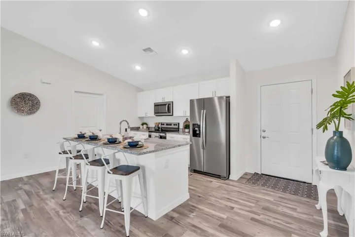 Kitchen featuring appliances with stainless steel finishes, white cabinetry, an island with sink, light wood-style floors, and a breakfast bar area
