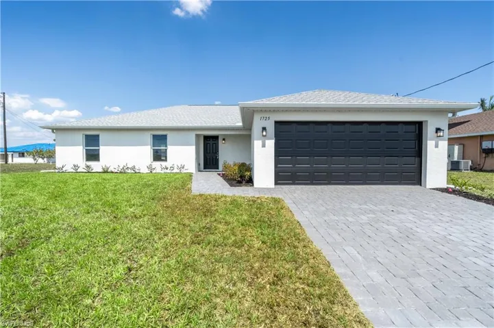 Ranch-style house with stucco siding, a front yard, decorative driveway, and a garage