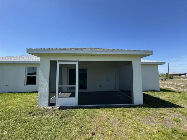 Rear view of property with stucco siding, a sunroom, and a lawn