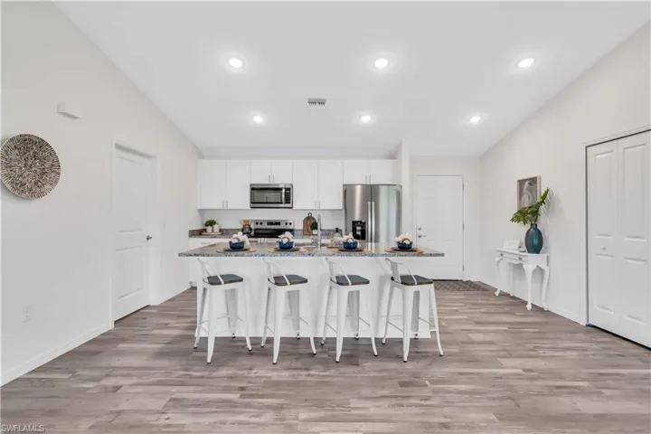 Kitchen featuring a breakfast bar, lofted ceiling, light stone counters, and appliances with stainless steel finishes