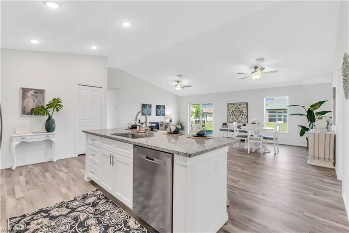 Kitchen with white cabinetry, vaulted ceiling, stainless steel dishwasher, a sink, and a ceiling fan