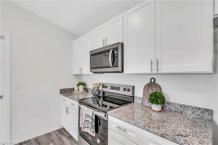 Kitchen with light stone countertops, light wood-type flooring, stainless steel appliances, baseboards, and white cabinets