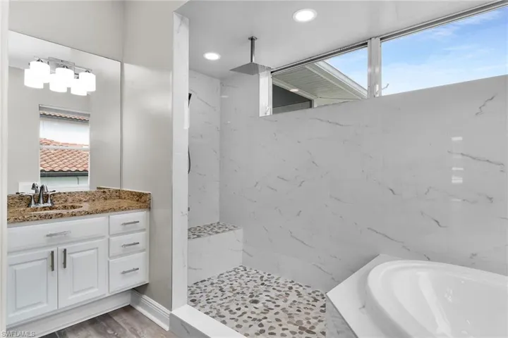 Bathroom featuring a marble finish shower, a garden tub, vanity, and recessed lighting