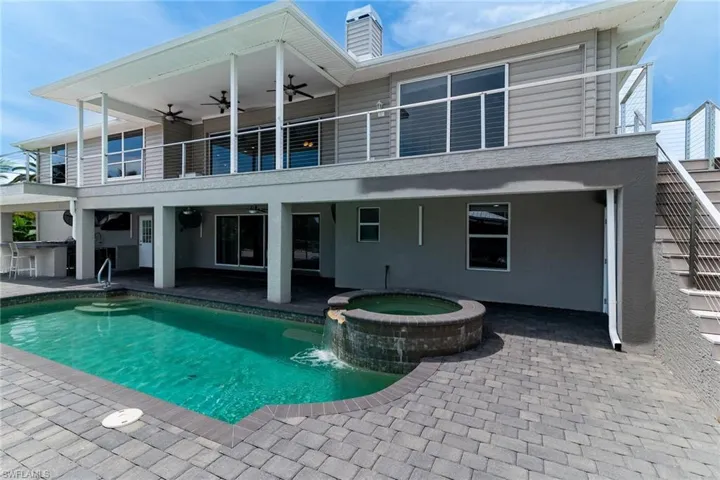 Rear view of property featuring a balcony, a patio, a ceiling fan, a pool with connected hot tub, and a chimney