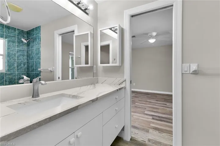 Full bath with vanity, wood finished floors, a ceiling fan, and a tile shower