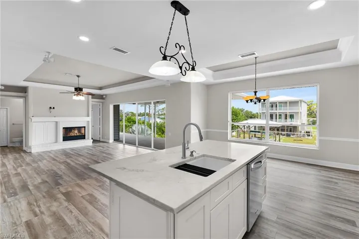 Kitchen with a raised ceiling, dishwasher, light wood-style flooring, a fireplace, and ceiling fan