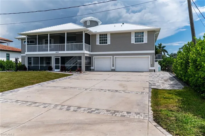 View of front facade with an attached garage, driveway, a front yard, stairway, and a metal roof