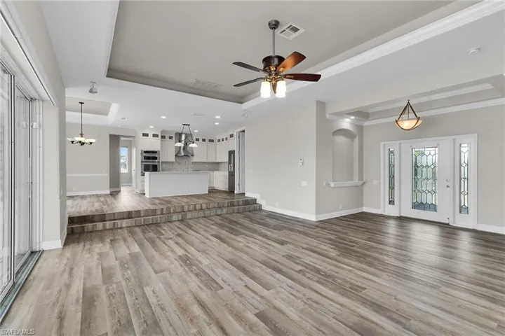 Unfurnished living room featuring a raised ceiling, wood finished floors, ornamental molding, ceiling fan, and recessed lighting