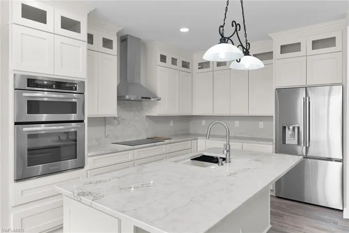 Kitchen with appliances with stainless steel finishes, wall chimney exhaust hood, an island with sink, pendant lighting, and recessed lighting