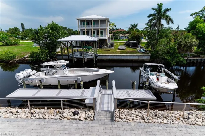 Dock area with boat lift, a water view, and a balcony