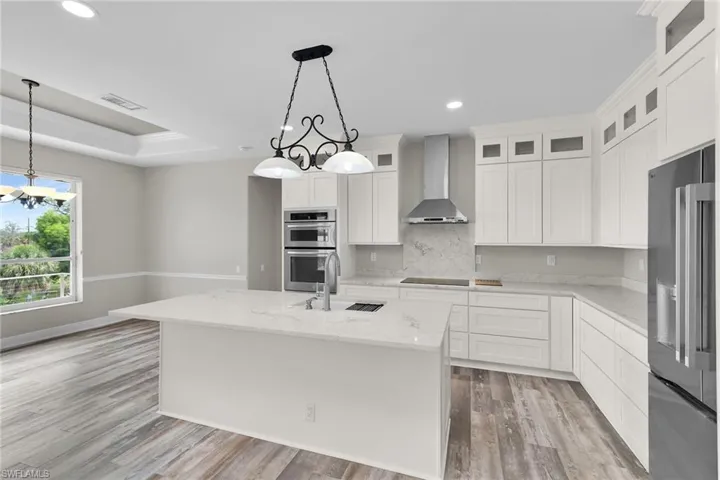 Kitchen with stainless steel appliances, wall chimney range hood, a chandelier, recessed lighting, and light wood finished floors