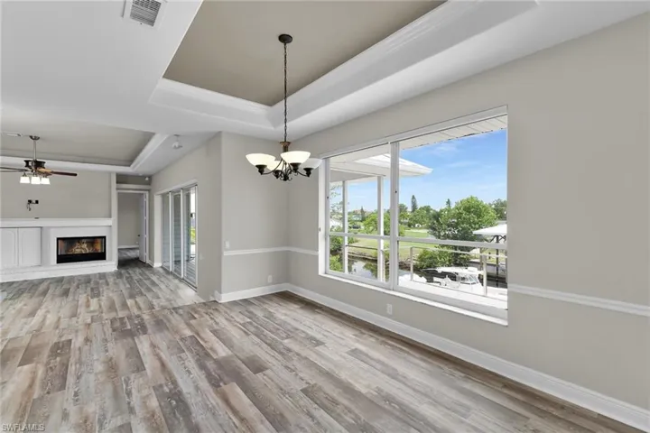 Unfurnished living room featuring a tray ceiling, a chandelier, wood finished floors, a ceiling fan, and a glass covered fireplace