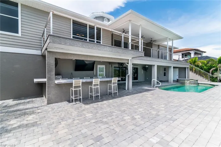Back of house featuring a bar, a balcony, a ceiling fan, a patio area, and a pool with connected hot tub