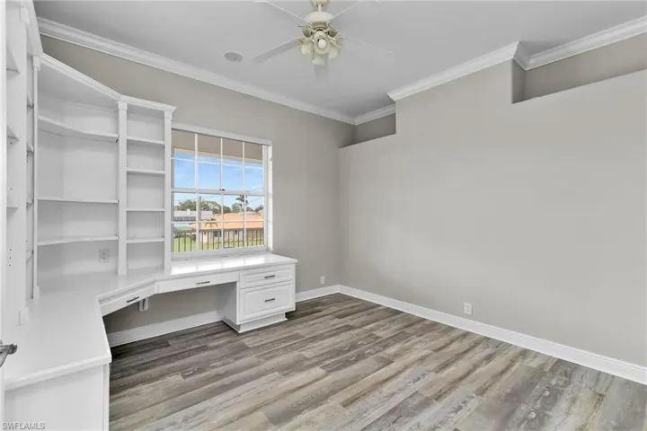 Unfurnished office featuring built in desk, ceiling fan, wood finished floors, and crown molding