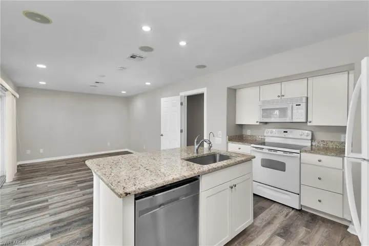 Kitchen featuring white appliances, wood finished floors, white cabinetry, light stone counters, and recessed lighting