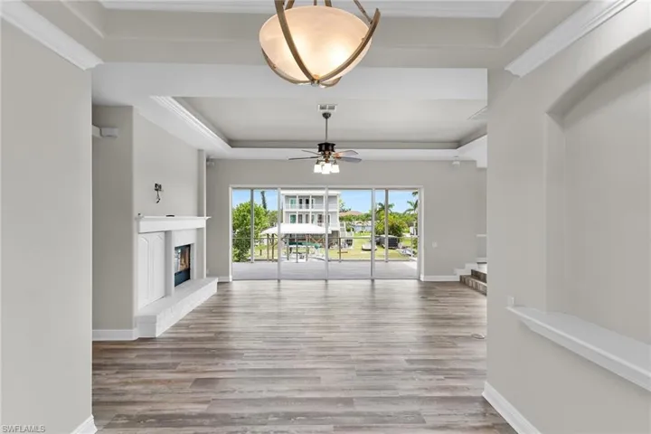Unfurnished living room featuring wood finished floors, a raised ceiling, a ceiling fan, a glass covered fireplace, and ornamental molding