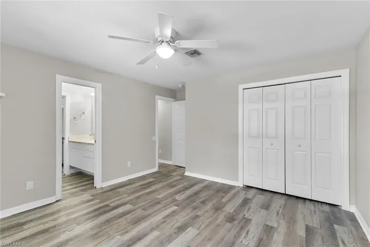 Unfurnished bedroom with wood finished floors, a closet, ceiling fan, and ensuite bathroom