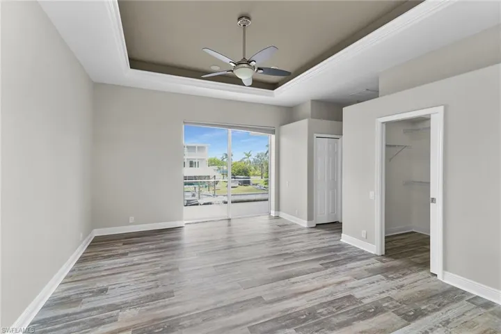 Unfurnished bedroom featuring a tray ceiling, access to outside, wood finished floors, and a ceiling fan