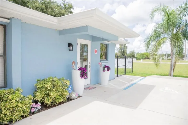 Light blue stucco exterior with white trim, featuring a glass-paneled entry door and an exterior wall light fixture