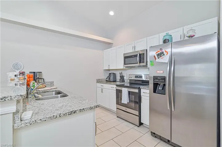 Kitchen with sink, white cabinetry, stainless steel appliances, lofted ceiling, and light stone counters