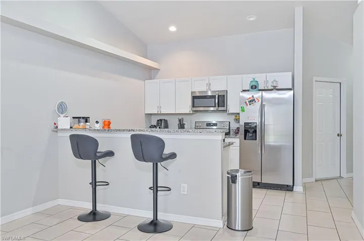 Kitchen with kitchen peninsula, stainless steel appliances, a breakfast bar, vaulted ceiling, and white cabinetry