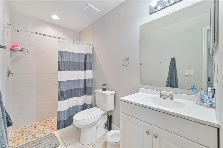 Bathroom with toilet, curtained shower, vanity, and tile patterned flooring