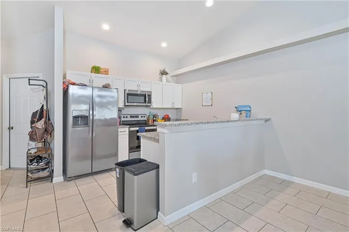 Kitchen with light stone countertops, appliances with stainless steel finishes, kitchen peninsula, white cabinetry, and vaulted ceiling