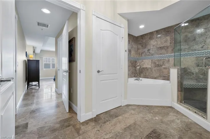 View from bathroom leading to bedroom with closet on right.  Oversized garden tub and linen closet.  Terrazzo tile throughout.