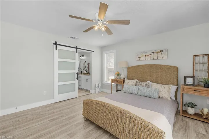 Bedroom with visible vents, baseboards, a barn door, ensuite bathroom, and light wood-style floors