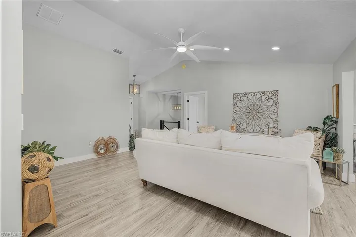 Living area with baseboards, visible vents, ceiling fan, vaulted ceiling, and light wood-style floors