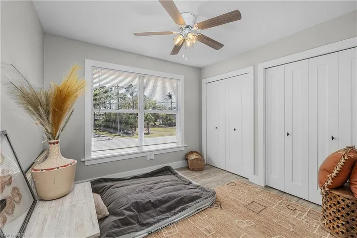 Bedroom with light wood finished floors, ceiling fan, two closets, and baseboards