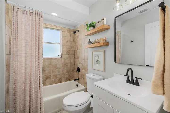 Bathroom featuring visible vents, toilet, vanity, and shower / bath combination with curtain
