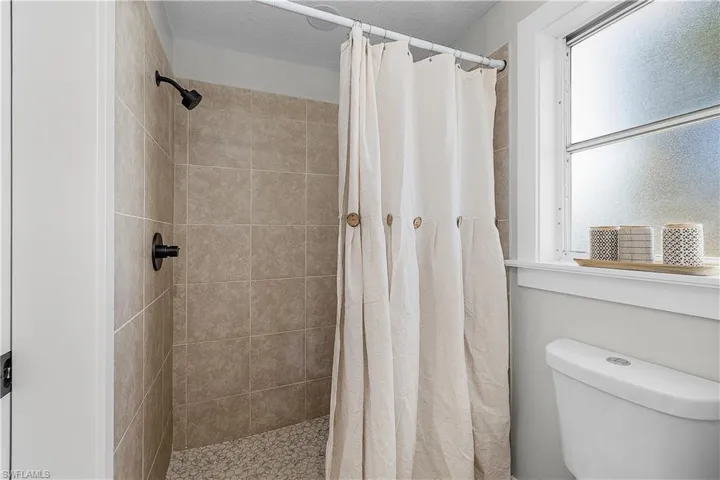 Full bath with a tile shower, toilet, and a textured ceiling