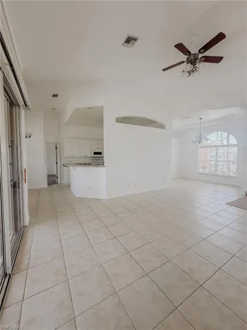 Unfurnished living room with light tile patterned floors, visible vents, and ceiling fan with notable chandelier