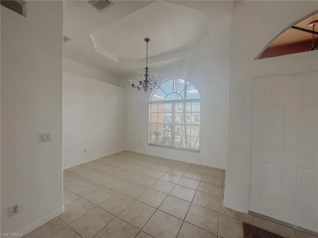 Unfurnished dining area with baseboards, a chandelier, light tile patterned flooring, visible vents, and a raised ceiling