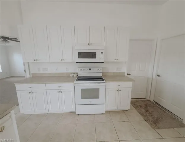 Kitchen with light countertops, white cabinets, white appliances, and light tile patterned flooring