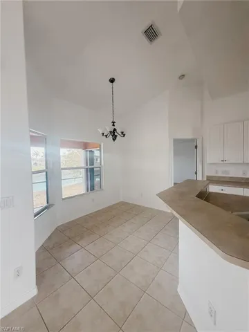 Unfurnished dining area with an inviting chandelier, lofted ceiling, visible vents, and light tile patterned floors